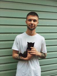 Portrait of young man with kitten standing against wall