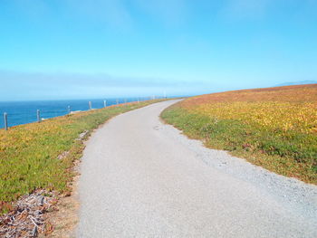 Road leading towards landscape against clear blue sky