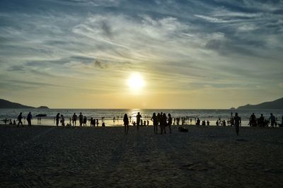 Silhouette people at beach against sky during sunset