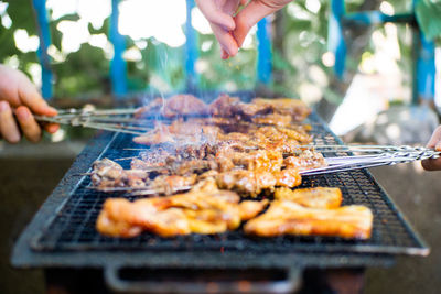 Cropped hands of people preparing food on barbecue grill