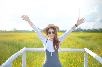Young woman wearing sunglasses with arms raised on field