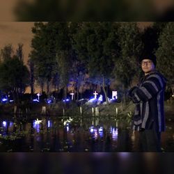 Portrait of young man standing by lake at night