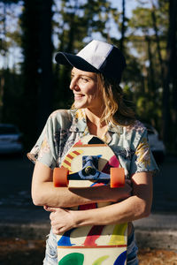 Cheerful woman looking away outdoors while holding skateboard