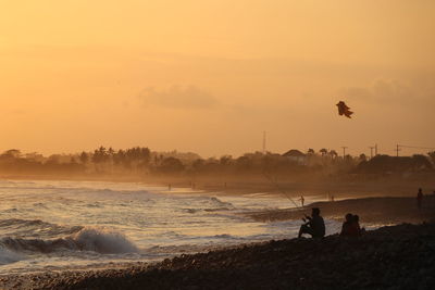 Silhouette man fishing on beach against sky during sunset