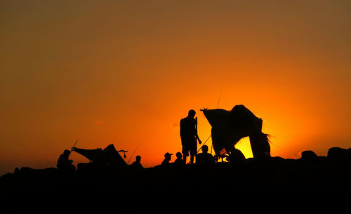 Silhouette friends camping on field against sky during sunset