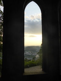 Silhouette trees and buildings seen through window during sunset