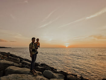 Man standing at sea shore against sky during sunset