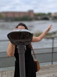 Woman looking through binoculars against railing and river