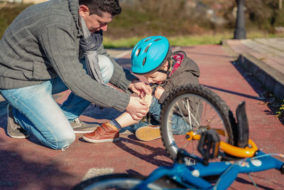 Father applying bandage on fallen son wound by bicycle on road