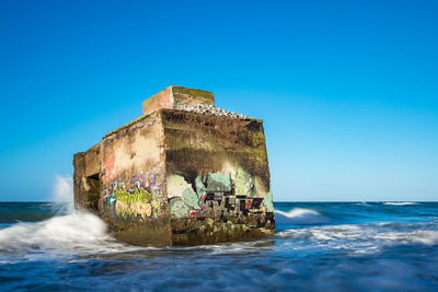 Built structure by sea against clear blue sky