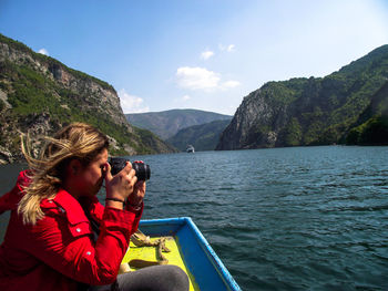 Woman photographing by mountains against sky