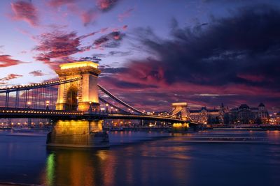 Illuminated bridge over river against sky in city at night