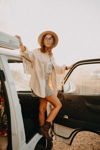 Portrait of young woman standing against car