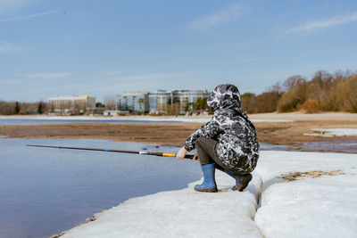 Cute little caucasian boy holding a fishing rod looking into distance on sea side on spring day