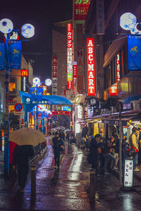 People walking on illuminated street during rainy season