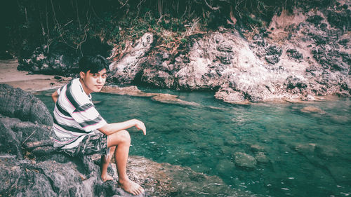 Portrait of young man sitting on rock by sea