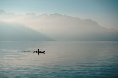 Silhouette person on boat sailing in sea against mountains