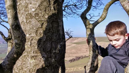 Close-up of boy on tree trunk against sky