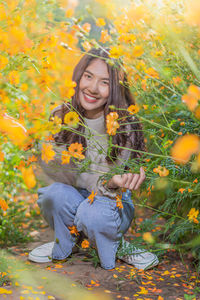 Full length portrait of woman crouching by yellow flowering plants