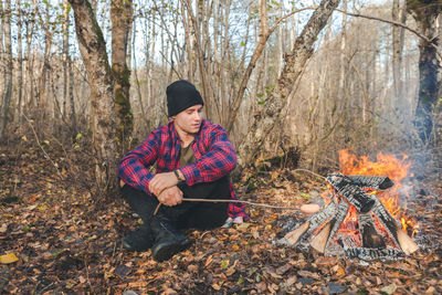 Full length of man sitting by campfire in forest during autumn