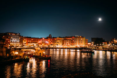 Illuminated buildings by river against sky at night