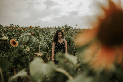 Young woman standing amidst sunflowers on field