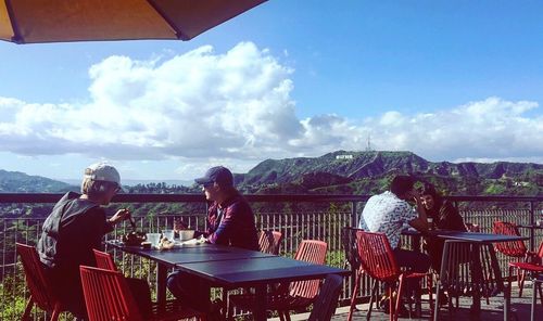 Rear view of people sitting on table against mountains