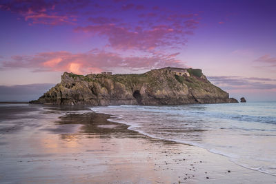 Rock formation on beach against sky during sunset