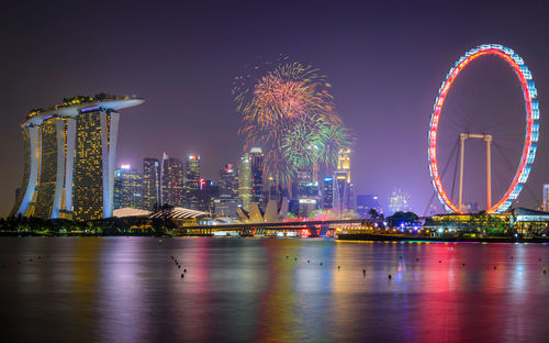 Illuminated singapore flyer and buildings by bay in city at night