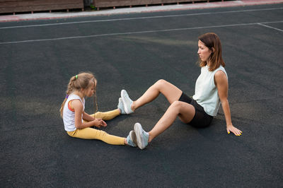 Woman with daughter sitting on footpath