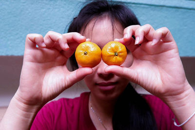 Close-up of woman holding orange over eyes