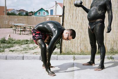 Man applying mud on body while standing by friend on footpath