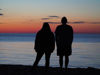 Rear view of silhouette couple standing on beach at sunset