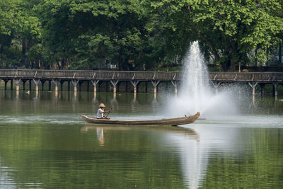 Man oaring boat by fountain on river