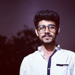 Portrait of young man wearing eyeglasses while standing against sky at night