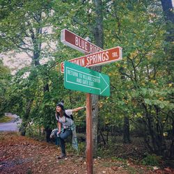 Woman standing by sign board on tree