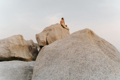 Rear view of naked man sitting on rock