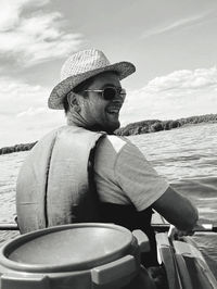 Man sitting by boat in sea against sky