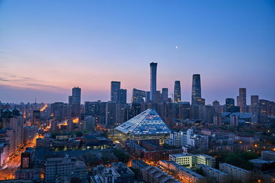 Illuminated buildings in city against sky during sunset