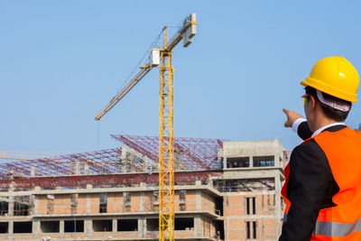 Side view of architect pointing towards crane at construction site