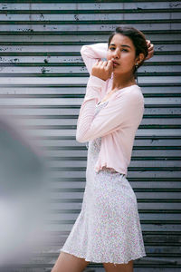 Young woman looking away while standing against wall