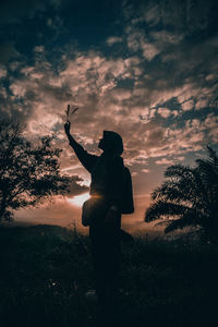 Silhouette man standing by tree on field against sky during sunset