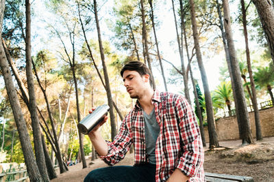 Young man looking away while sitting on tree trunk in forest