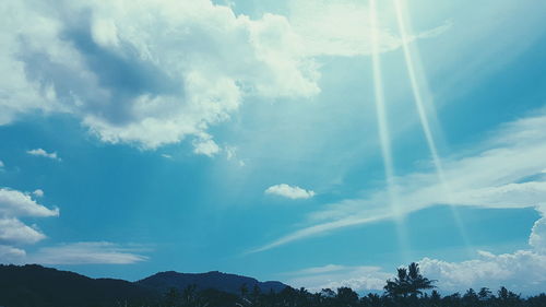 Low angle view of sunlight streaming through clouds