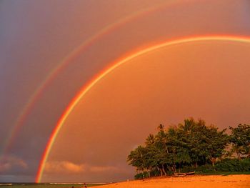 Scenic view of rainbow over sea against sky at sunset