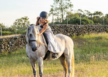 Lusitano horse, white mare, female rider, outdoors on pasture.