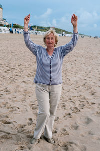 Portrait of senior woman with arms raised standing at beach