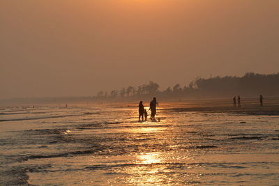Silhouette people on beach against sky during sunset