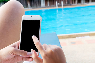 Midsection of woman using smart phone at poolside