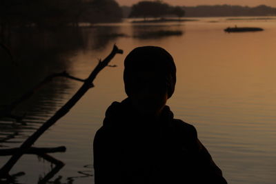 Rear view of silhouette boy standing at lake during sunset